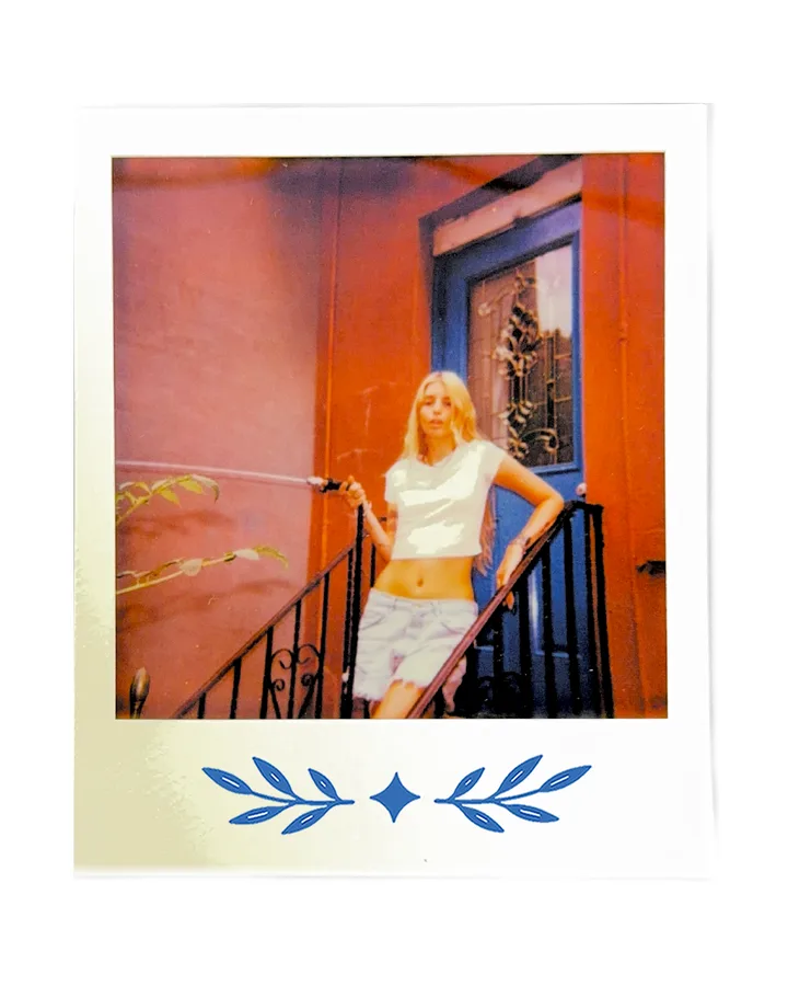 A member on a stoop beside a blue door, in the Zari tee.