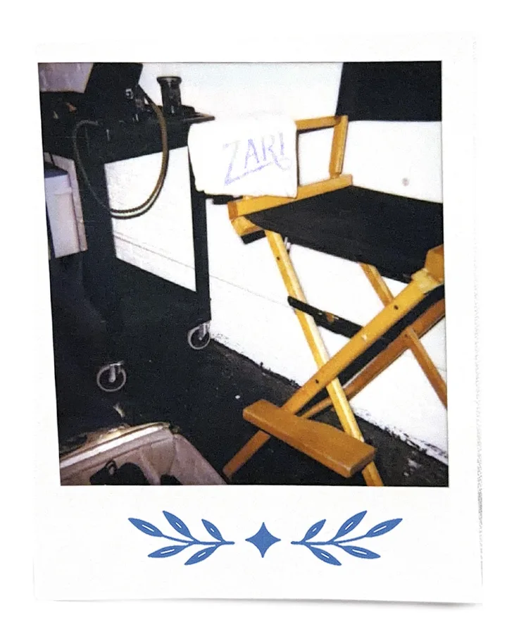 A director's chair on set, a Zari towel hung over the back.