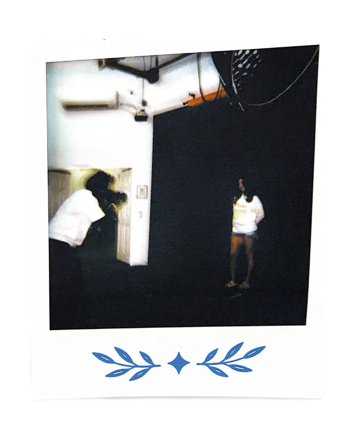 Two figures on a studio set, lights and a white wall.
