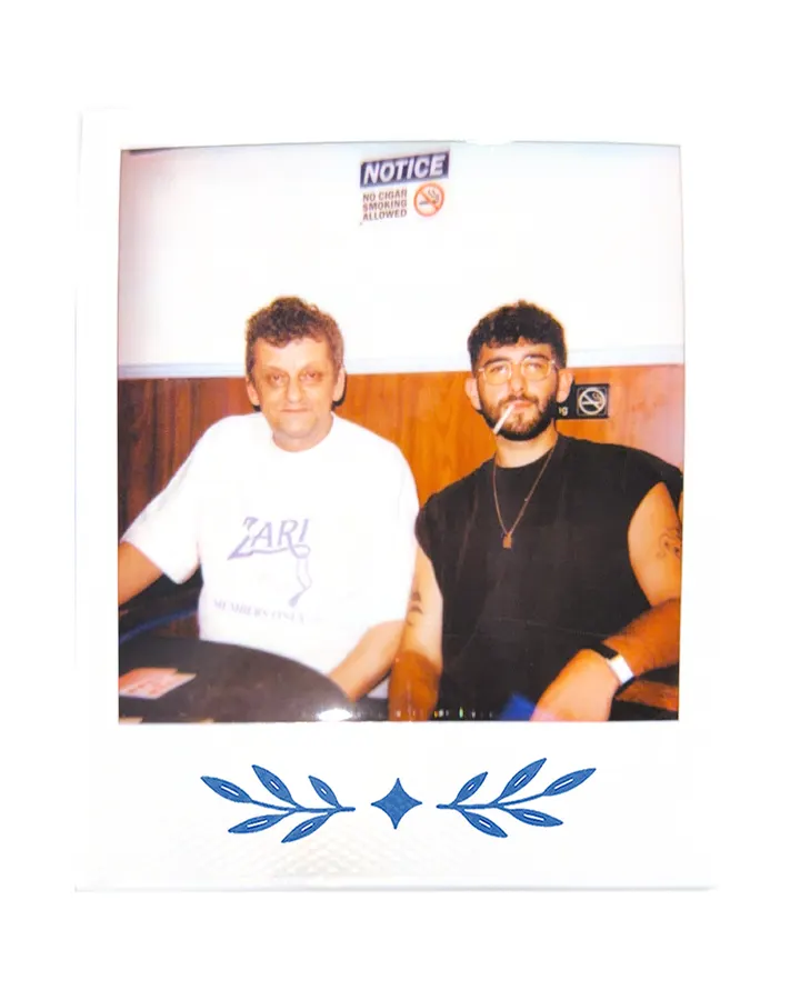 Two members at a table under a notice sign, one in the Zari tee.