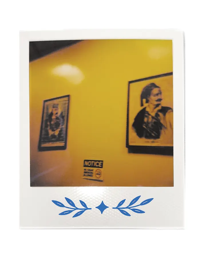 A yellow wall with two framed portraits and a notice.