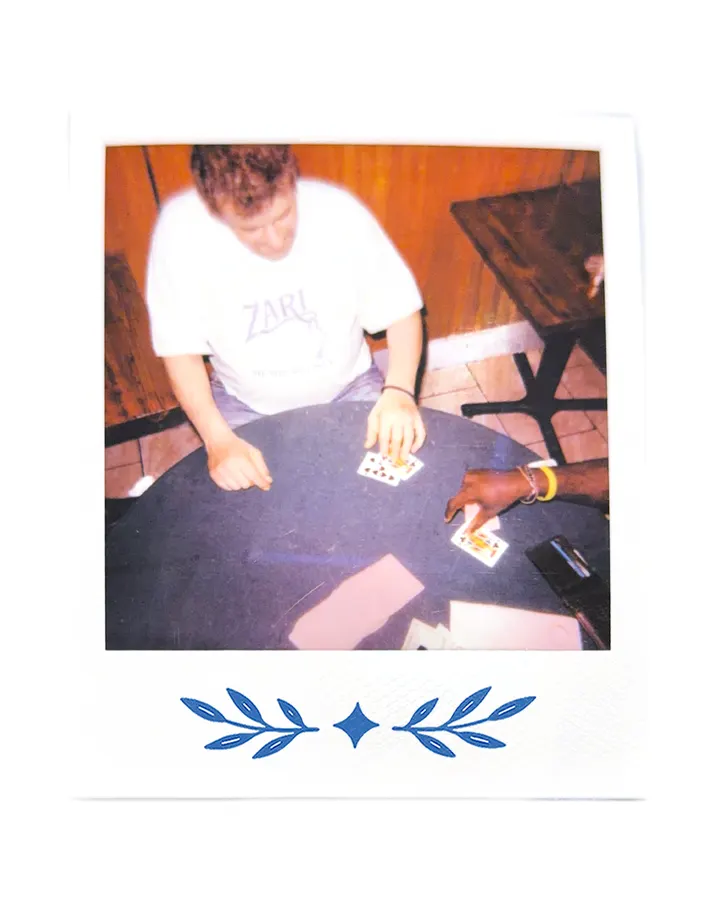 A member in the Zari tee bent over a hand of cards.