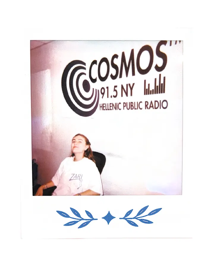 A member seated at the studio desk in the Zari tee, the Cosmos FM sign above.